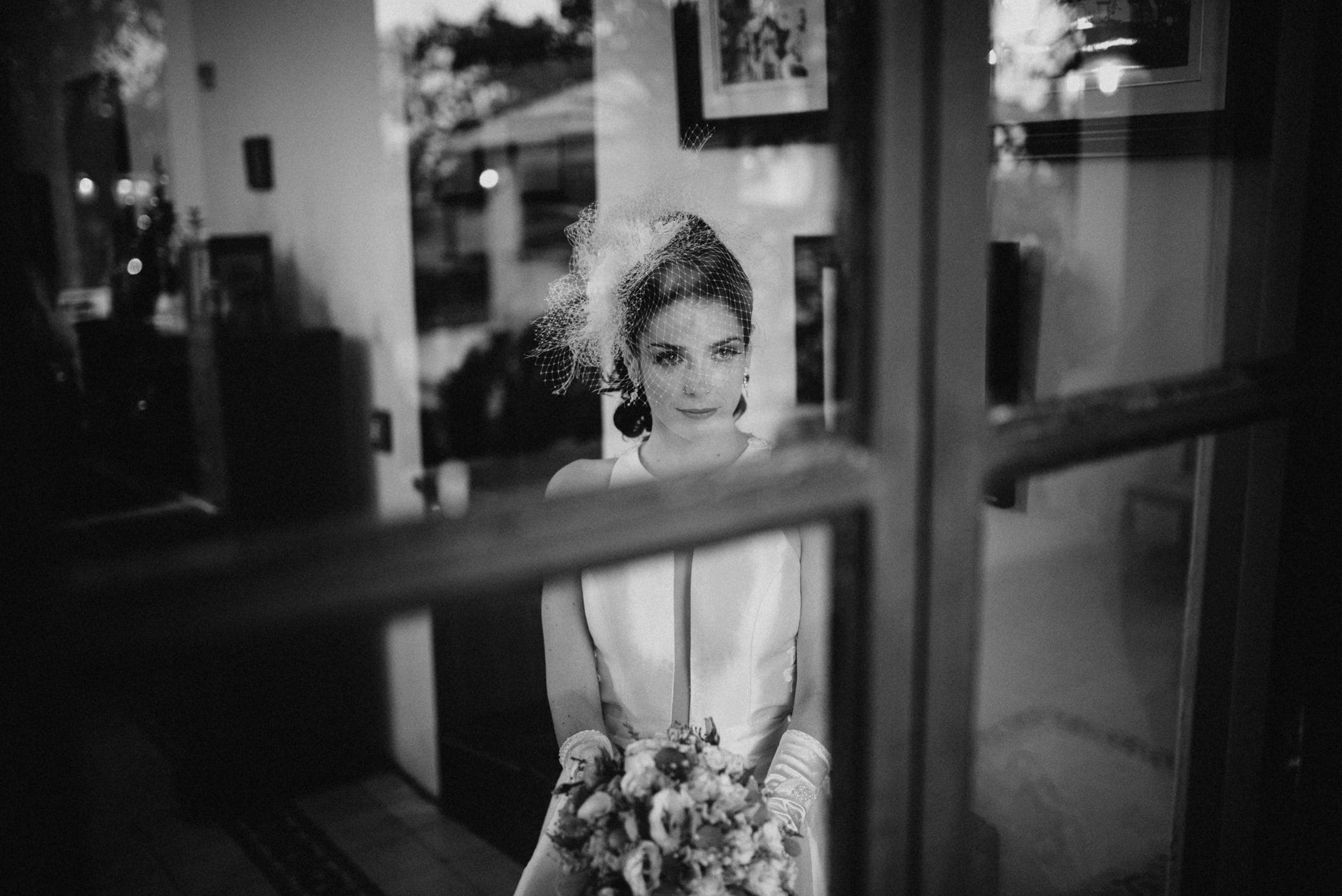 A bride framed in a window at dusk, holding her bouquet