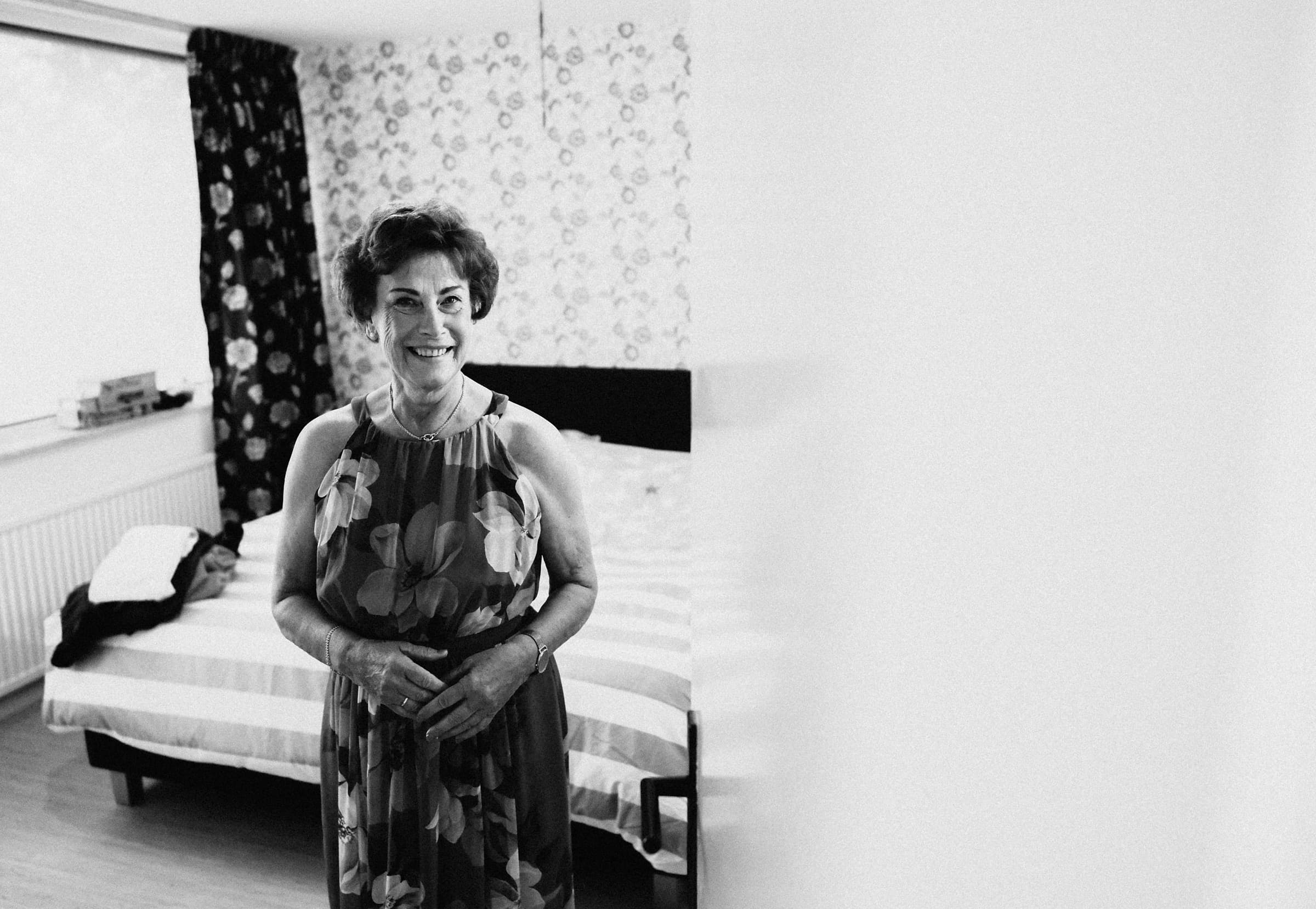 A black and white candid portrait of the groom's mother smiling while getting ready before the wedding
