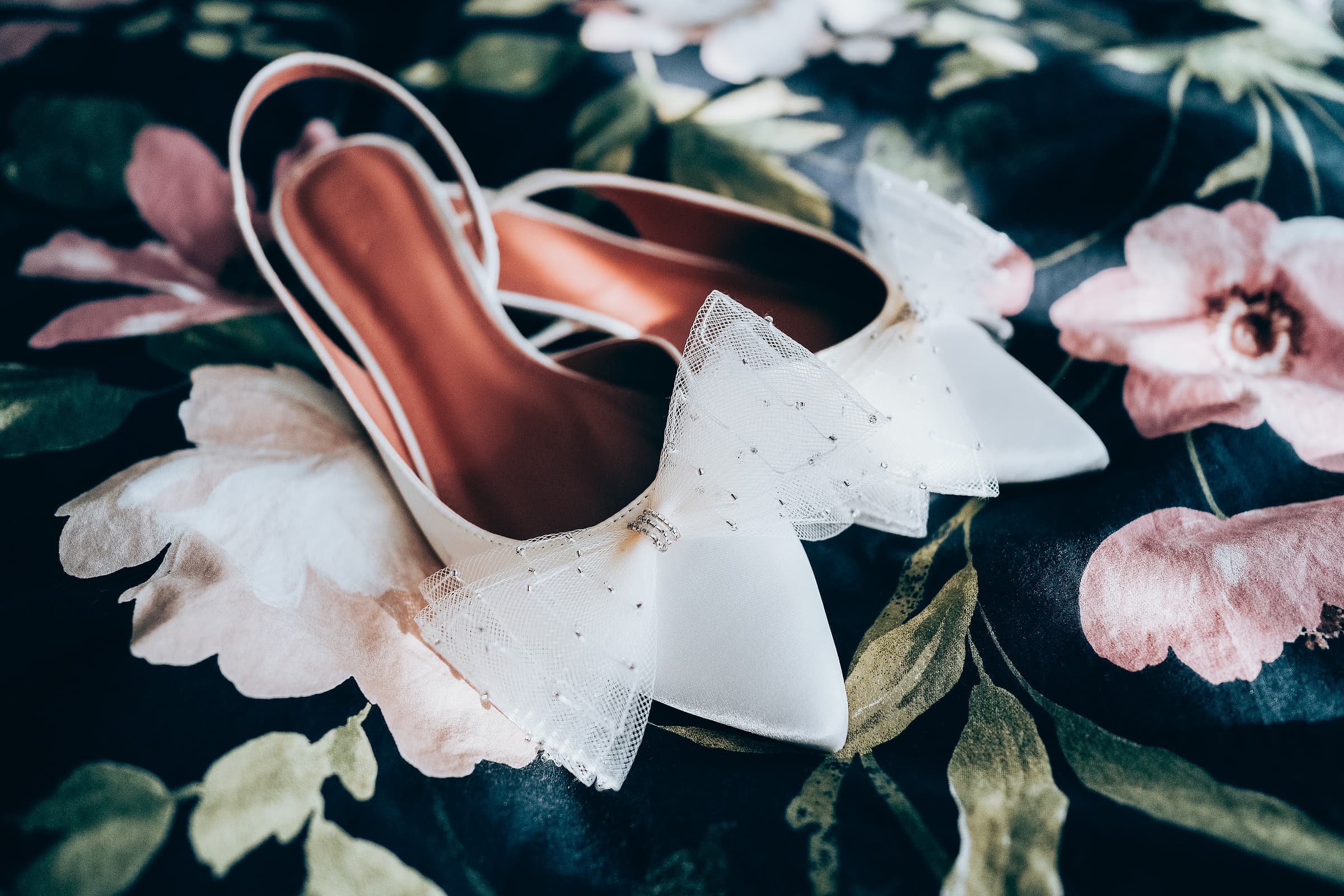 A close-up detail shot of wedding shoes resting on a floral fabric backdrop