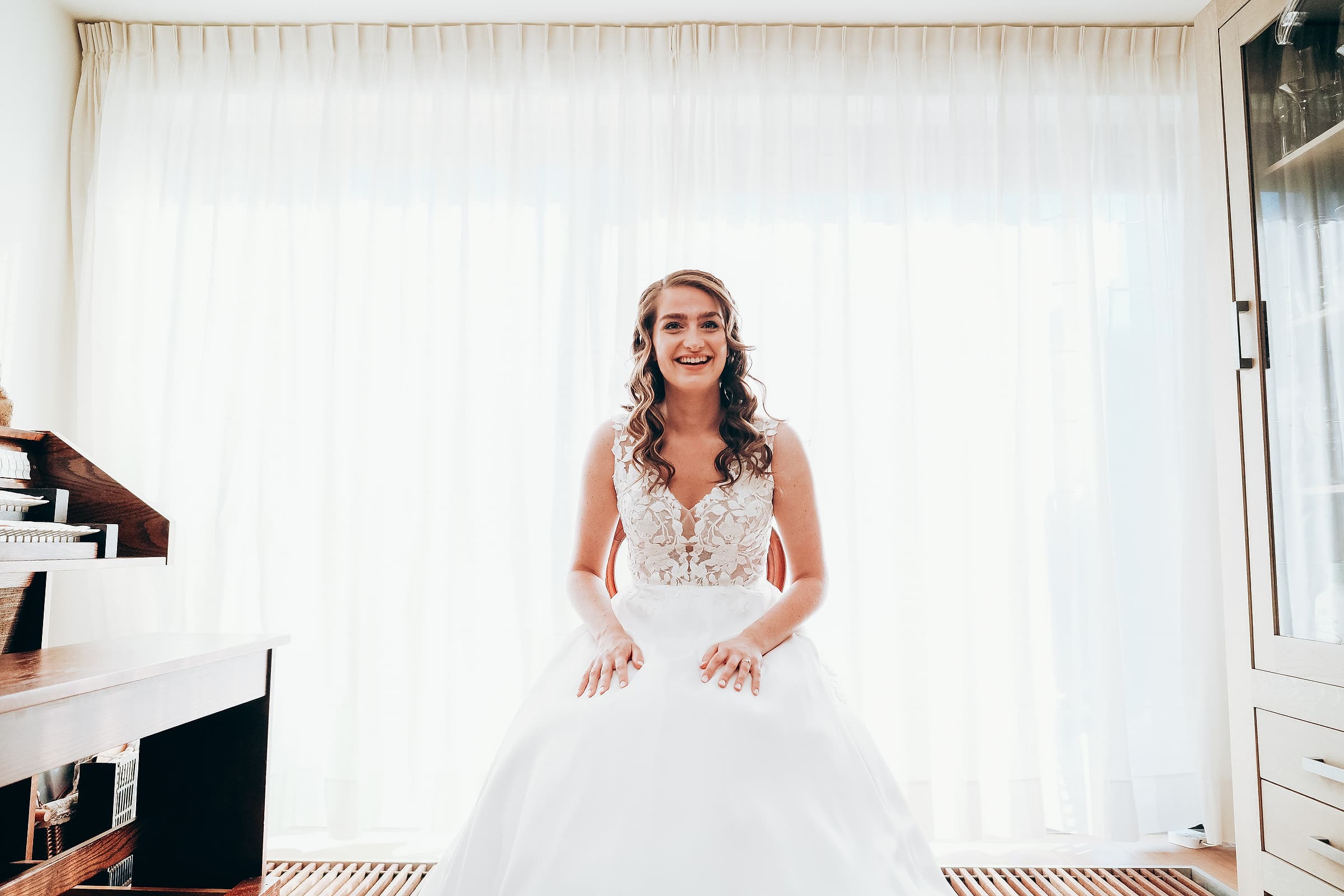 A bride sitting and laughing in soft window light before the ceremony