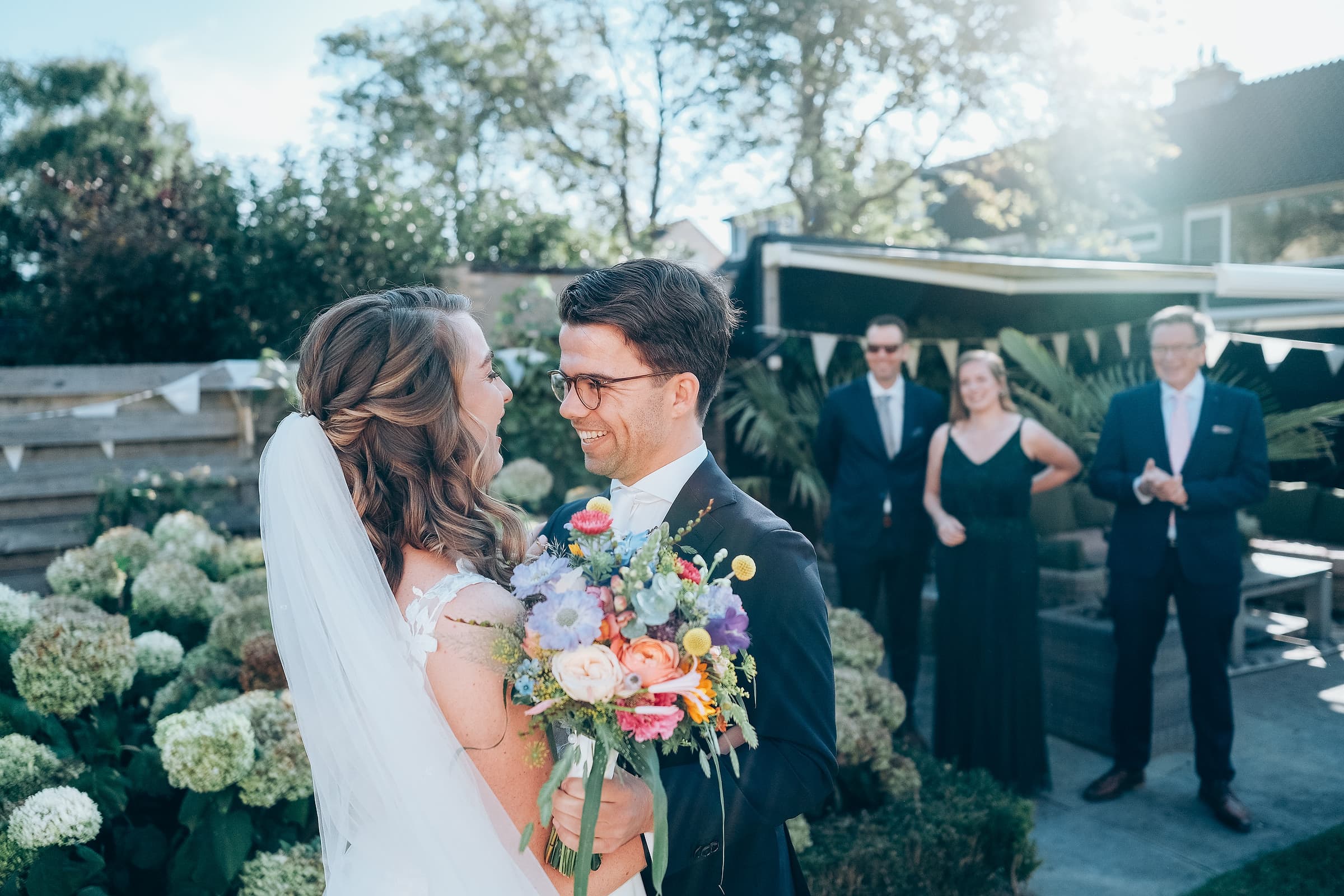 A bride and groom laughing together as wedding guests applaud behind them