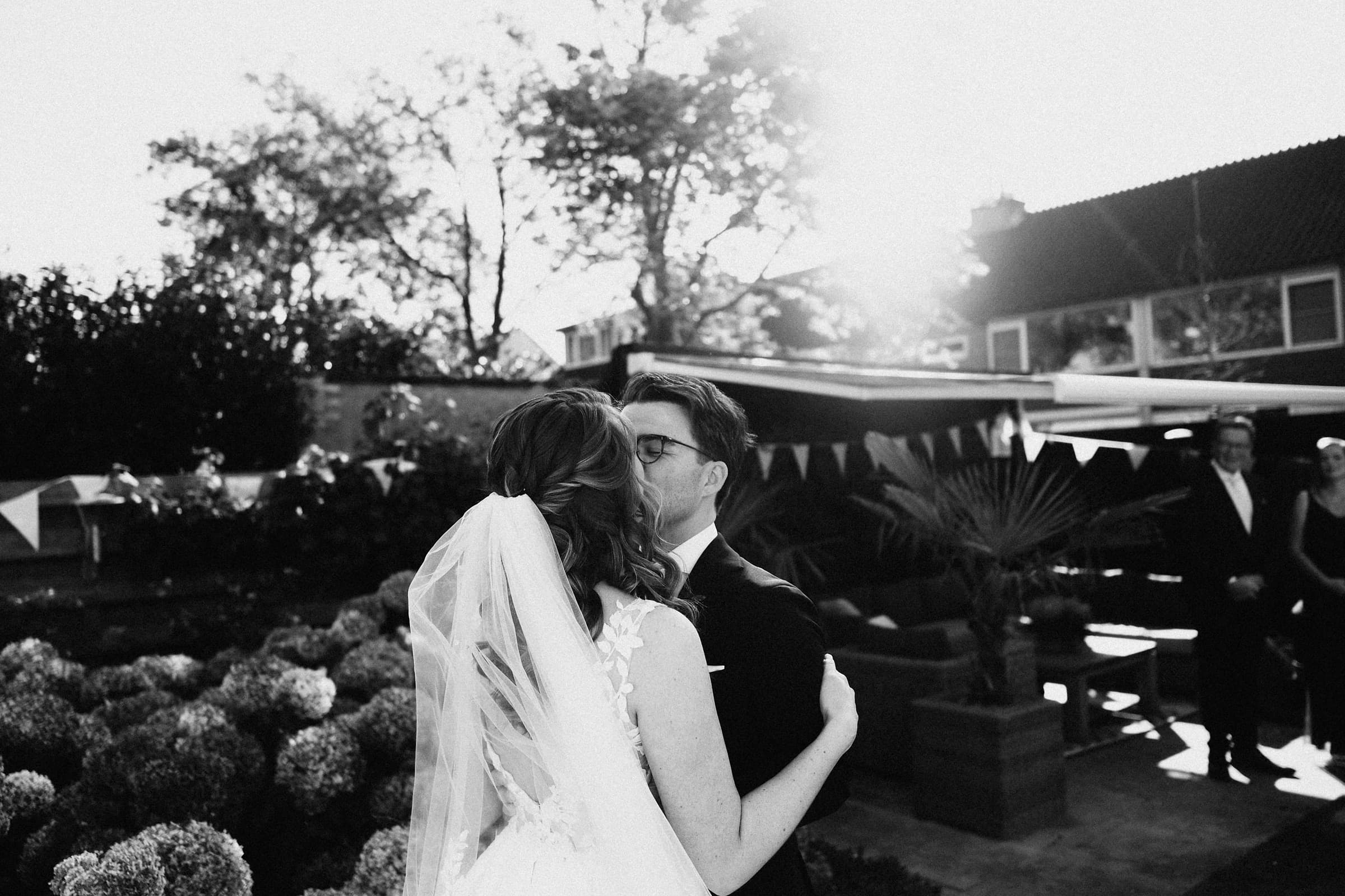 A bride and groom embracing at golden hour while wedding guests look on