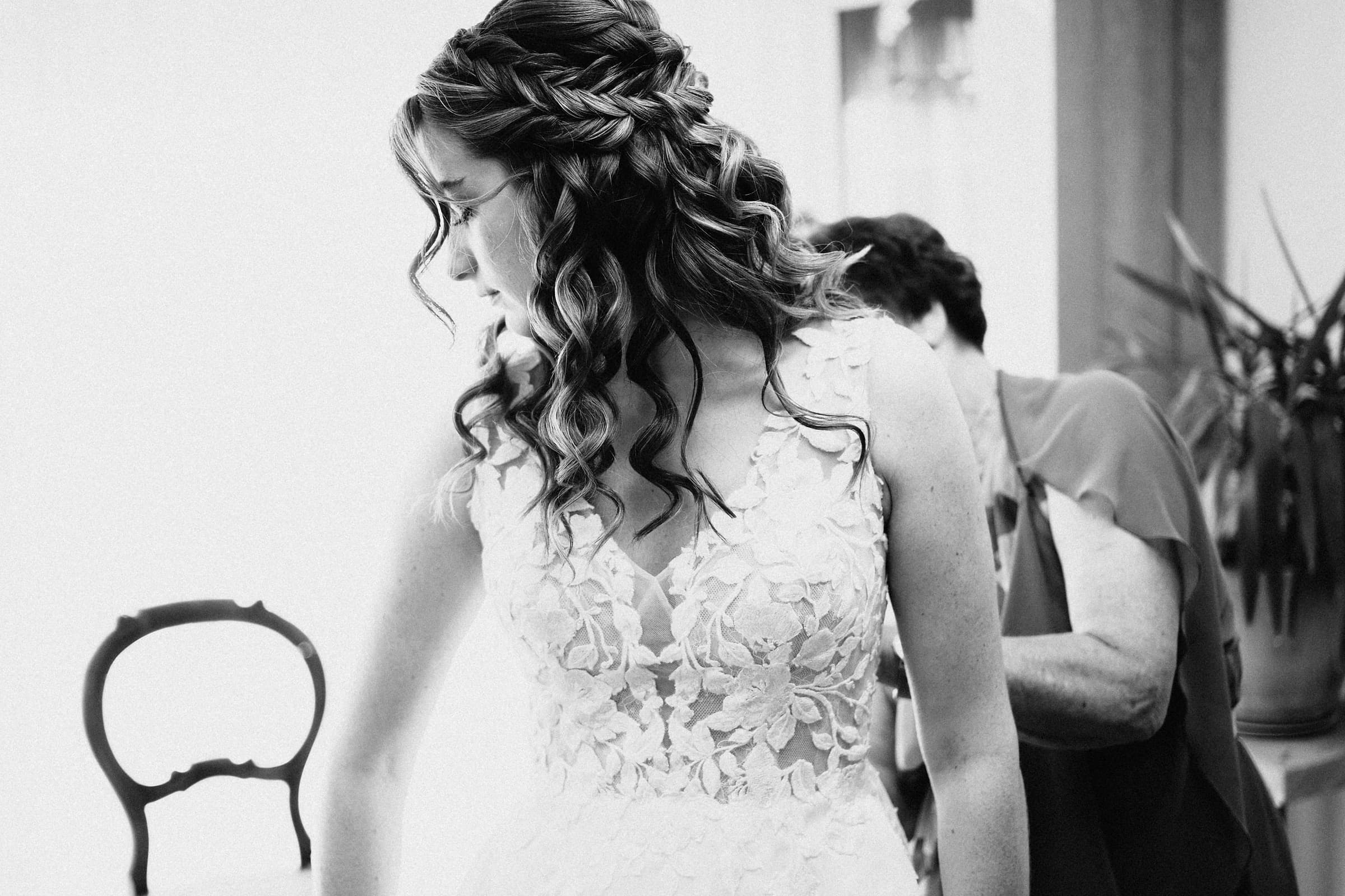 A black and white detail portrait of a bride's braided hair and lace wedding gown