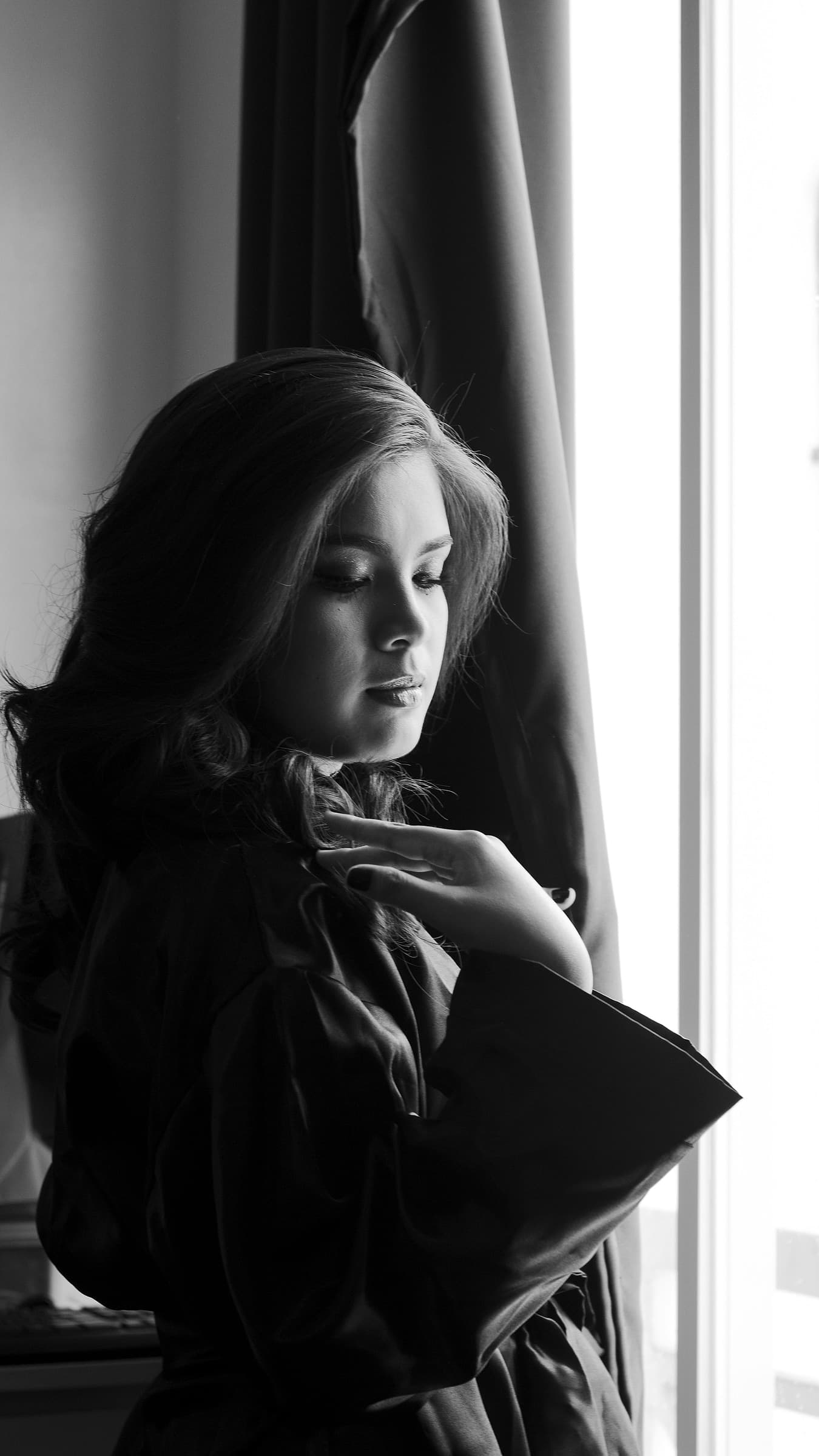 A person in a silk robe standing in soft window light, photographed in black and white