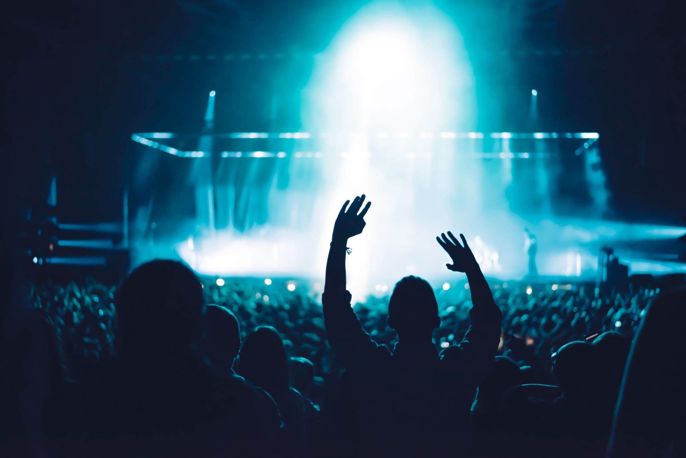 A concert crowd with hands raised in silhouette against bright blue stage light