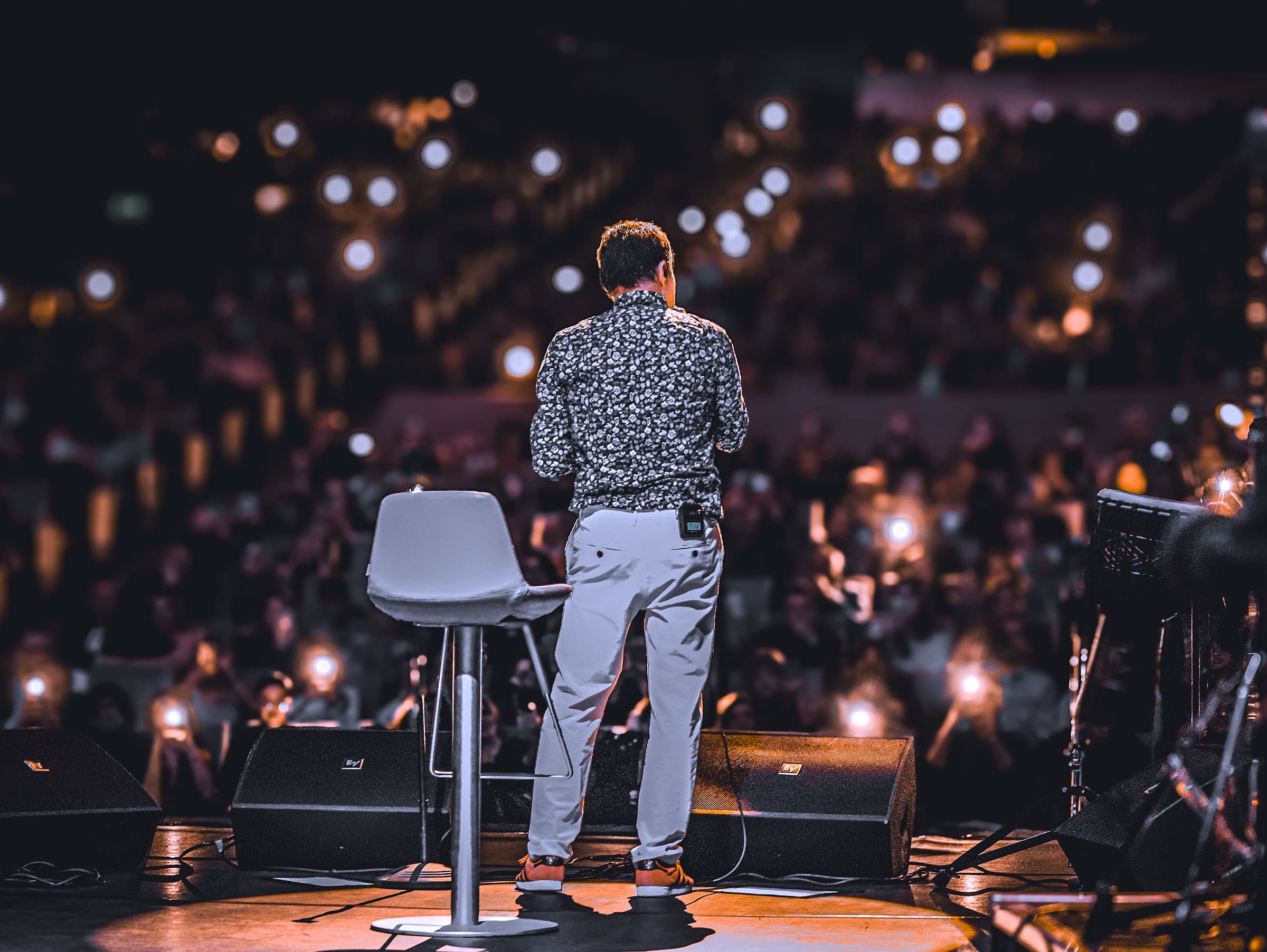 A speaker on stage in front of a lit audience at a corporate conference, photographed from behind the stage