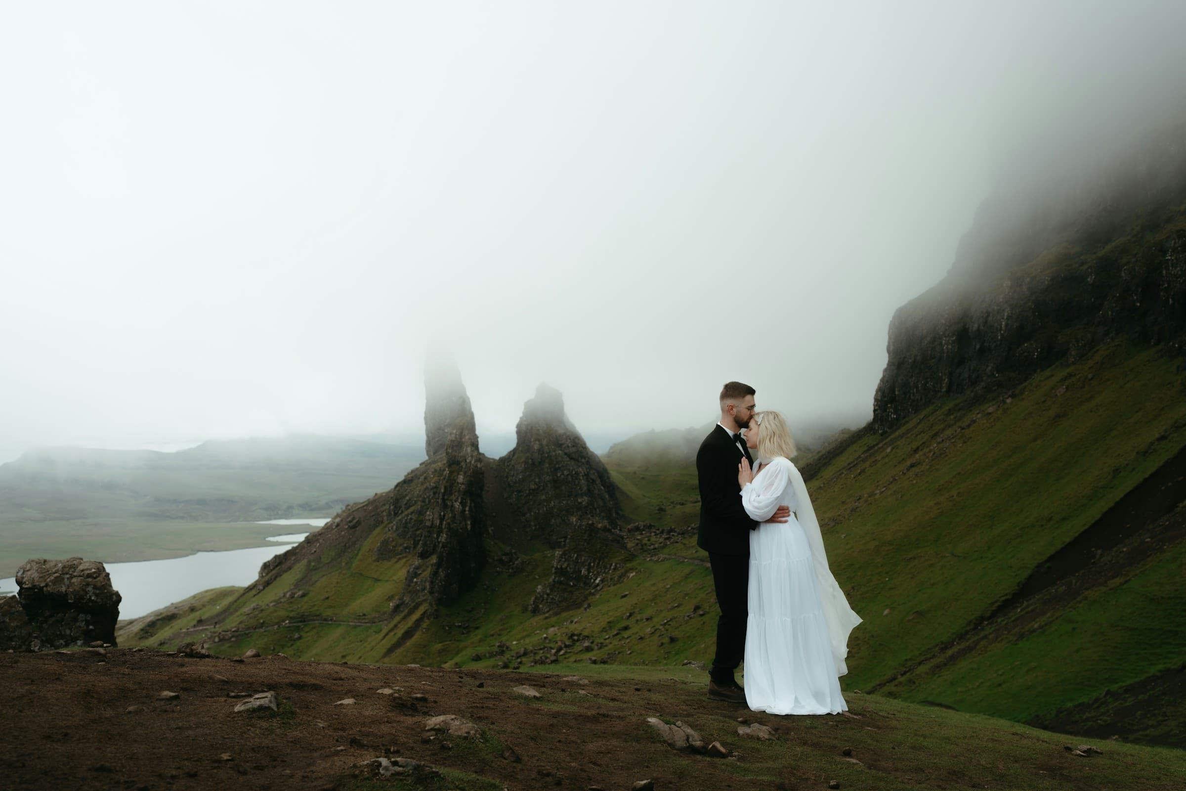 A couple in wedding attire standing together on a misty mountain ridge in Scotland