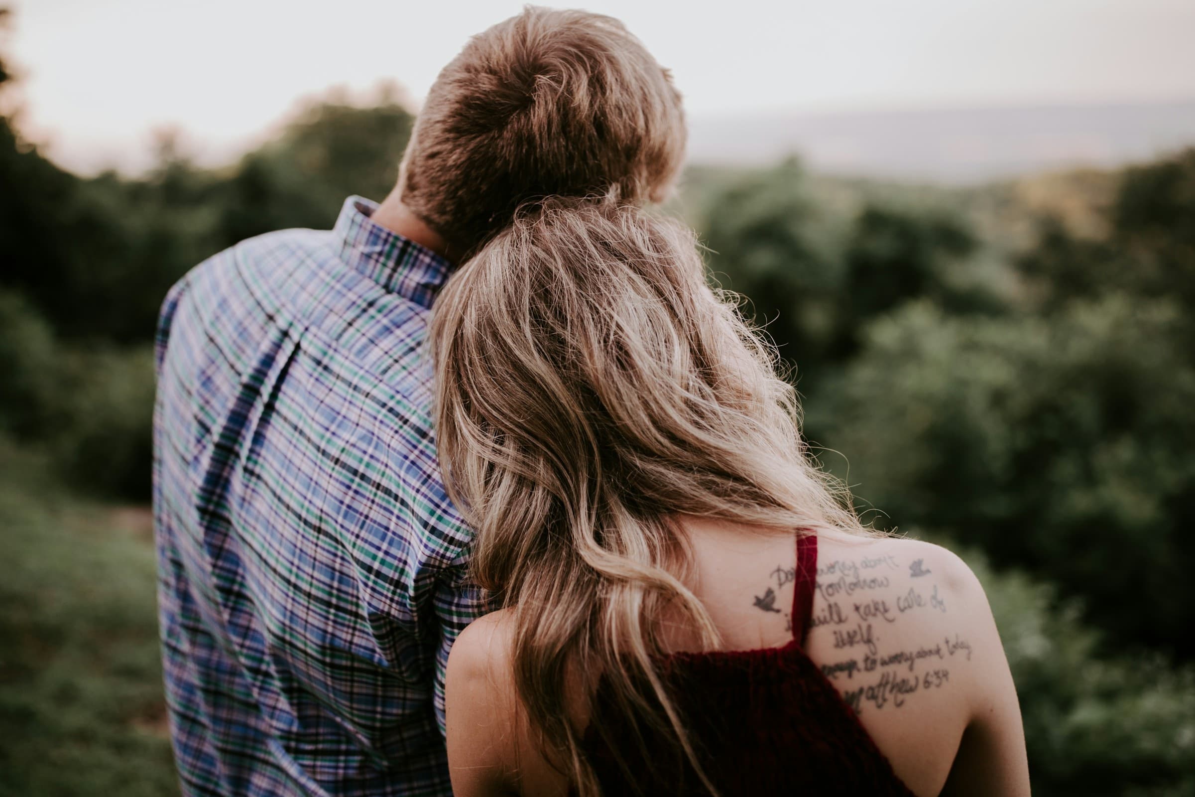 An engaged couple standing close together on a hillside in warm evening light