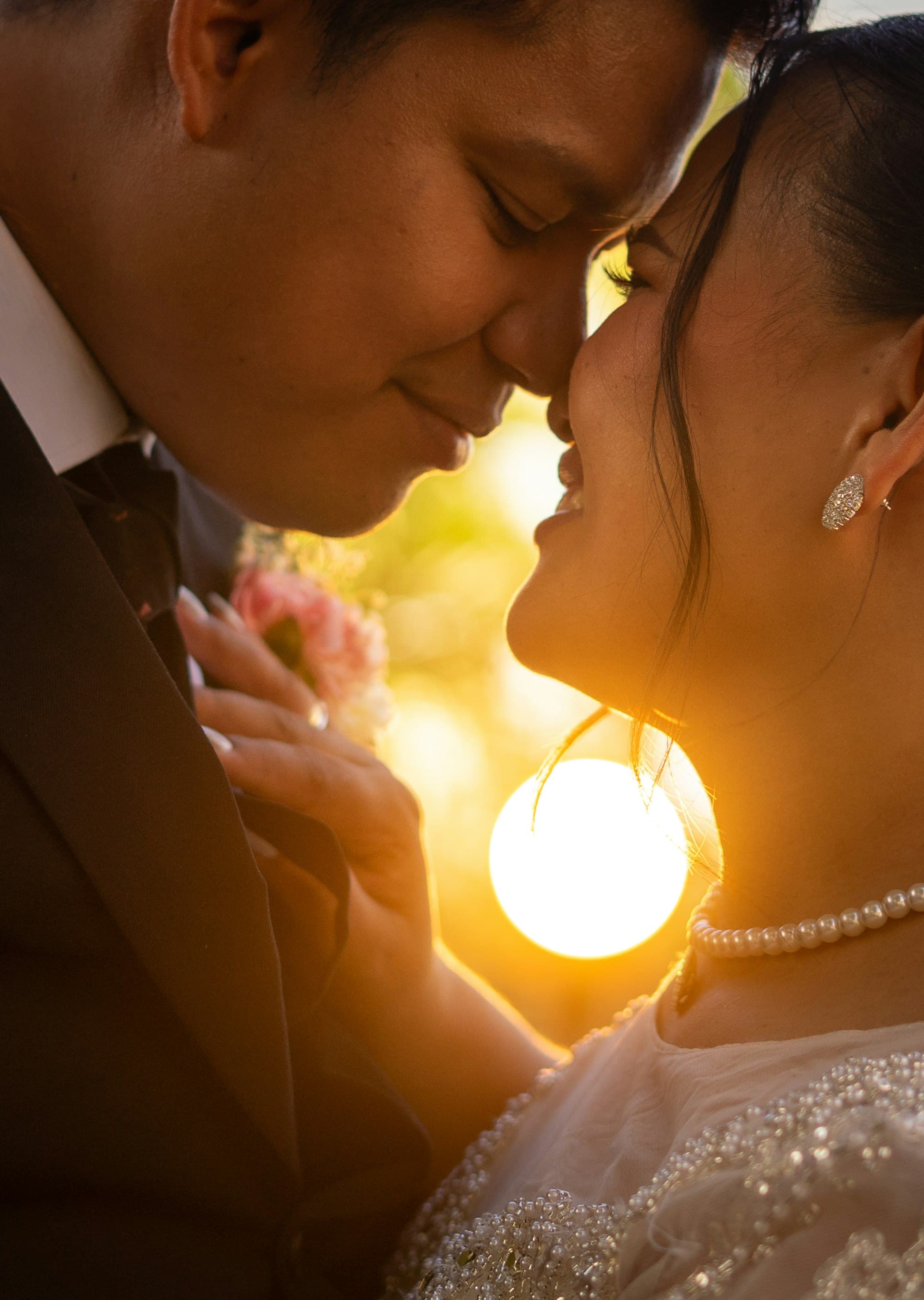 A bride and groom nose to nose in silhouette, backlit by a bright golden sunset