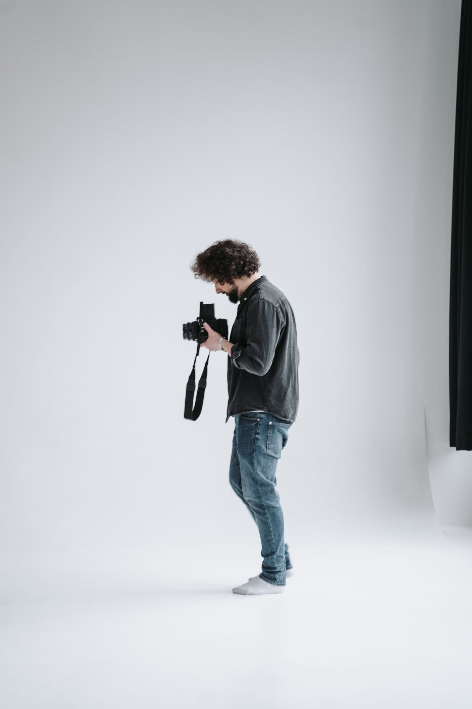 A photographer in a minimalist white studio checking a camera during a portrait session