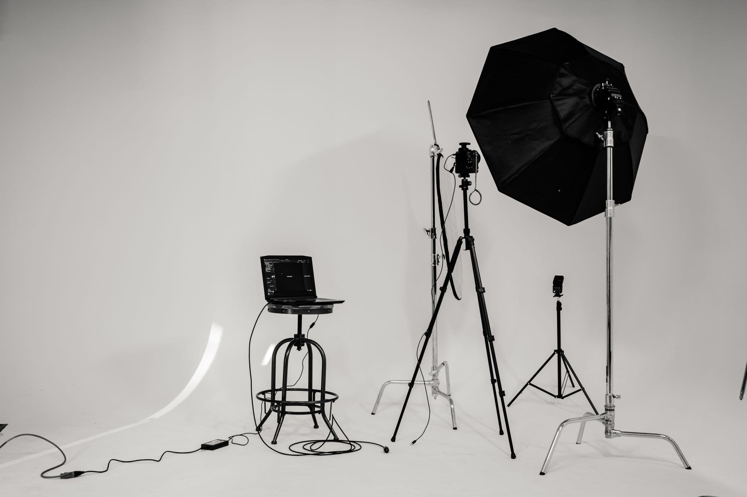 A professional headshot studio setup with a large octabox softbox, light stands and a tethered laptop against a white backdrop