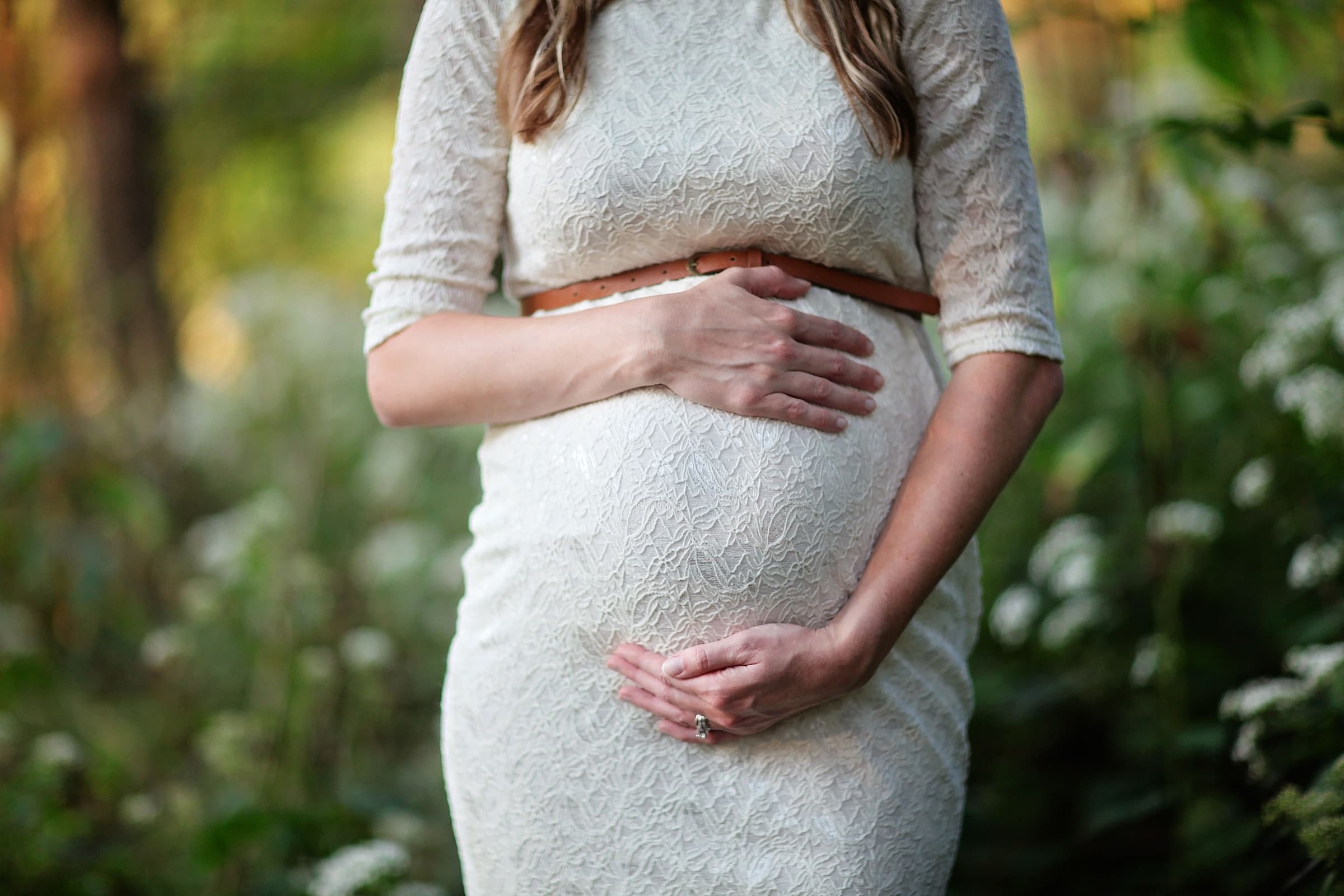 A pregnant woman in a lace dress resting her hands on her bump during an outdoor maternity session in soft evening light