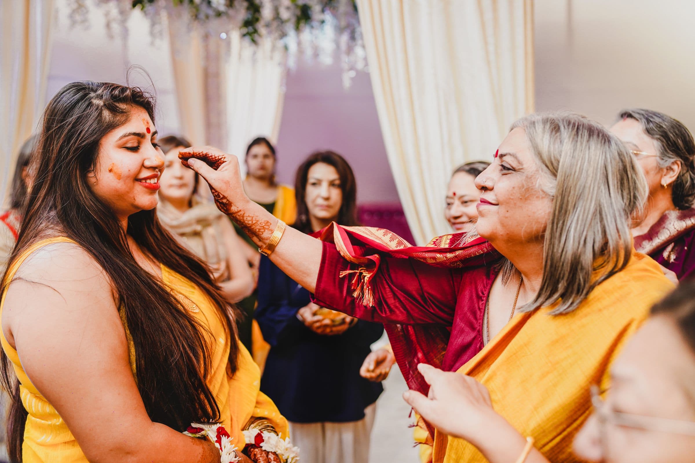 Two women in bright yellow and red traditional dress laughing during a Haldi ceremony ahead of a multi-day wedding