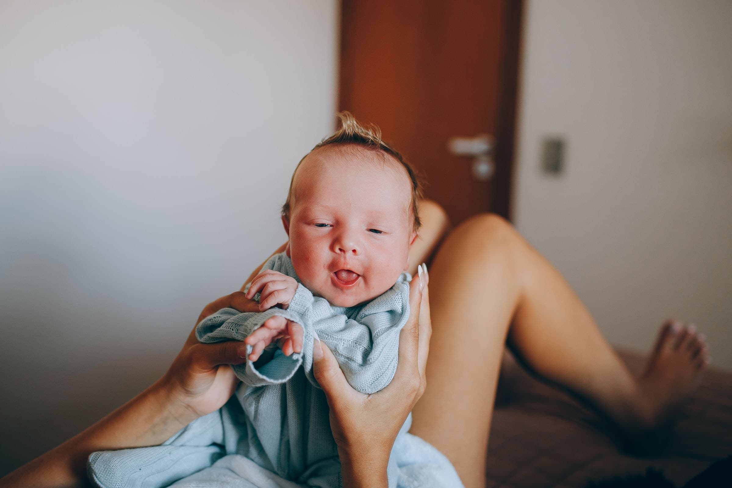 A newborn baby held in a parent's hands on a bed in soft natural light