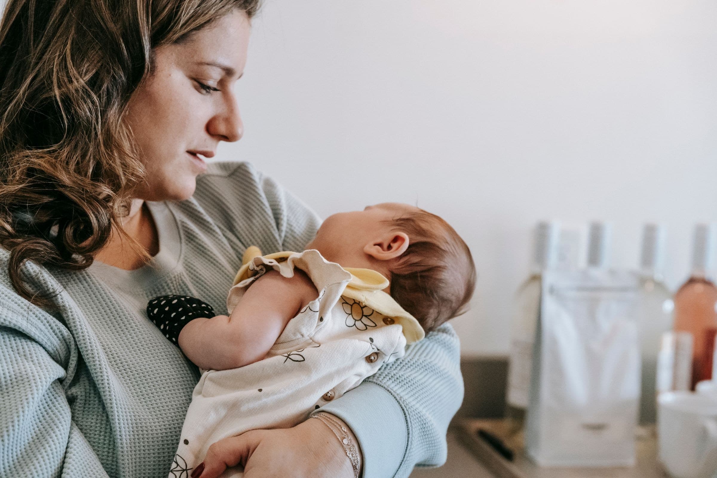 A mother holding her newborn baby in soft window light during a lifestyle newborn session