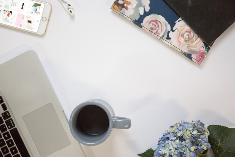 A laptop, phone, coffee mug, and a floral notebook laid out on a desk before a call