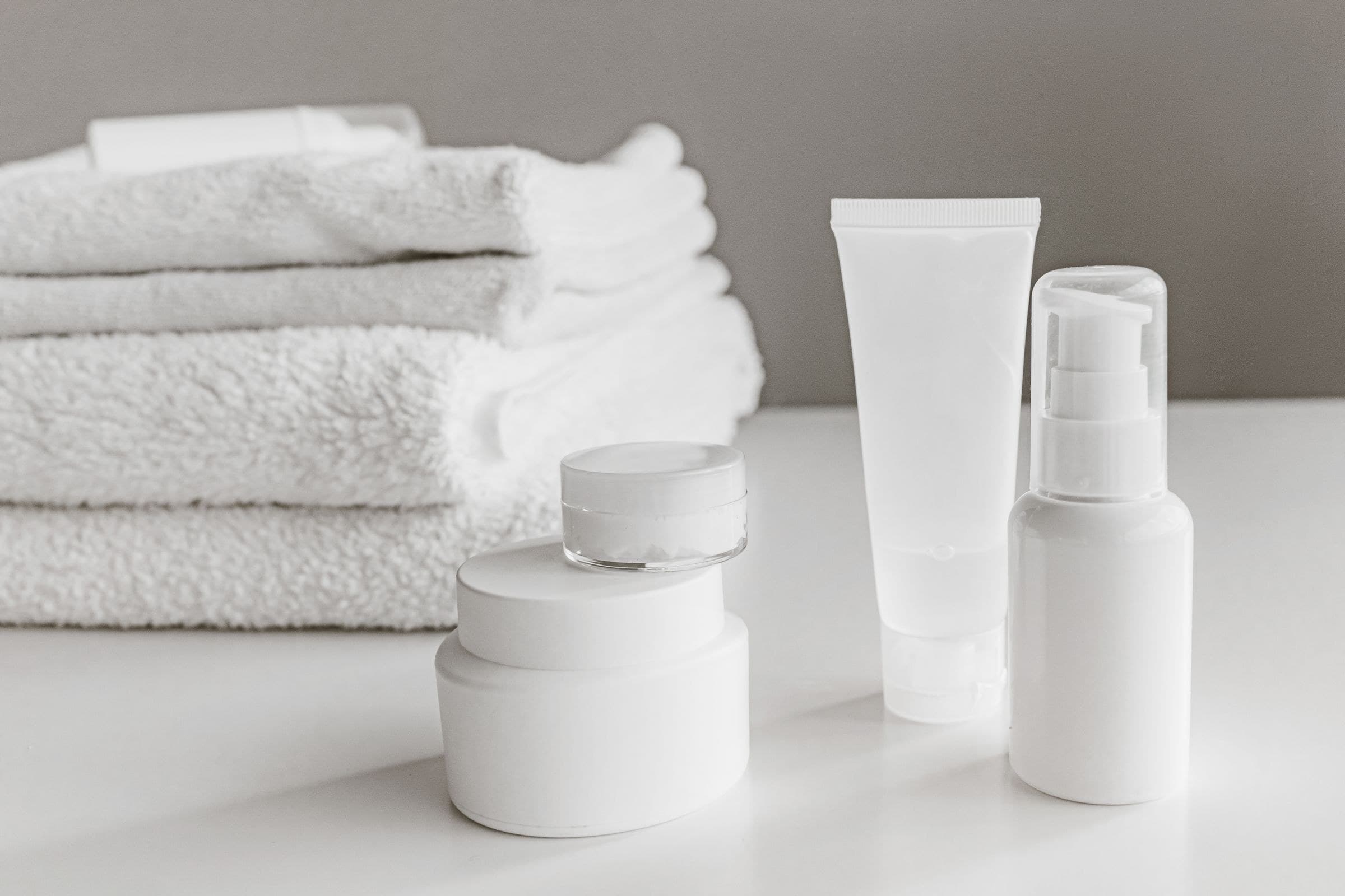 Clean white skincare bottles and jars arranged on a white surface with folded towels for an e-commerce listing