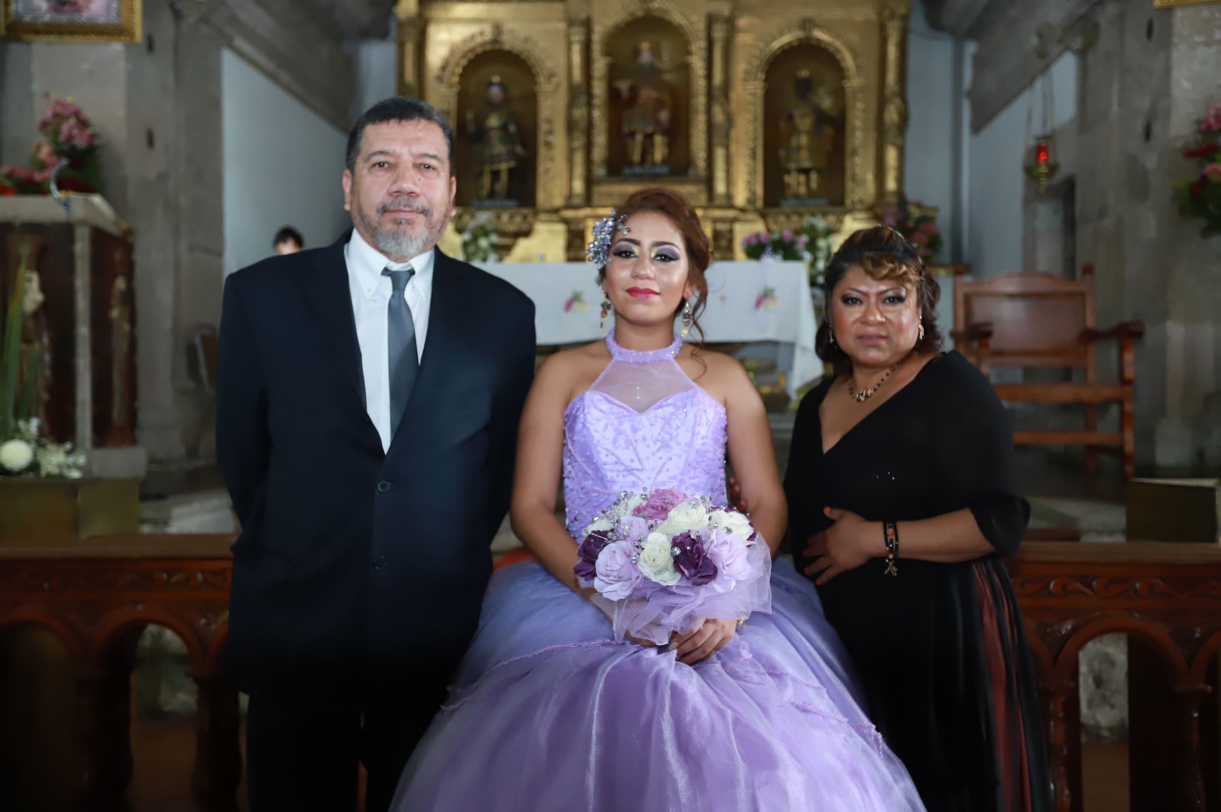 A quinceañera standing with her parents in a decorated church after the thanksgiving mass