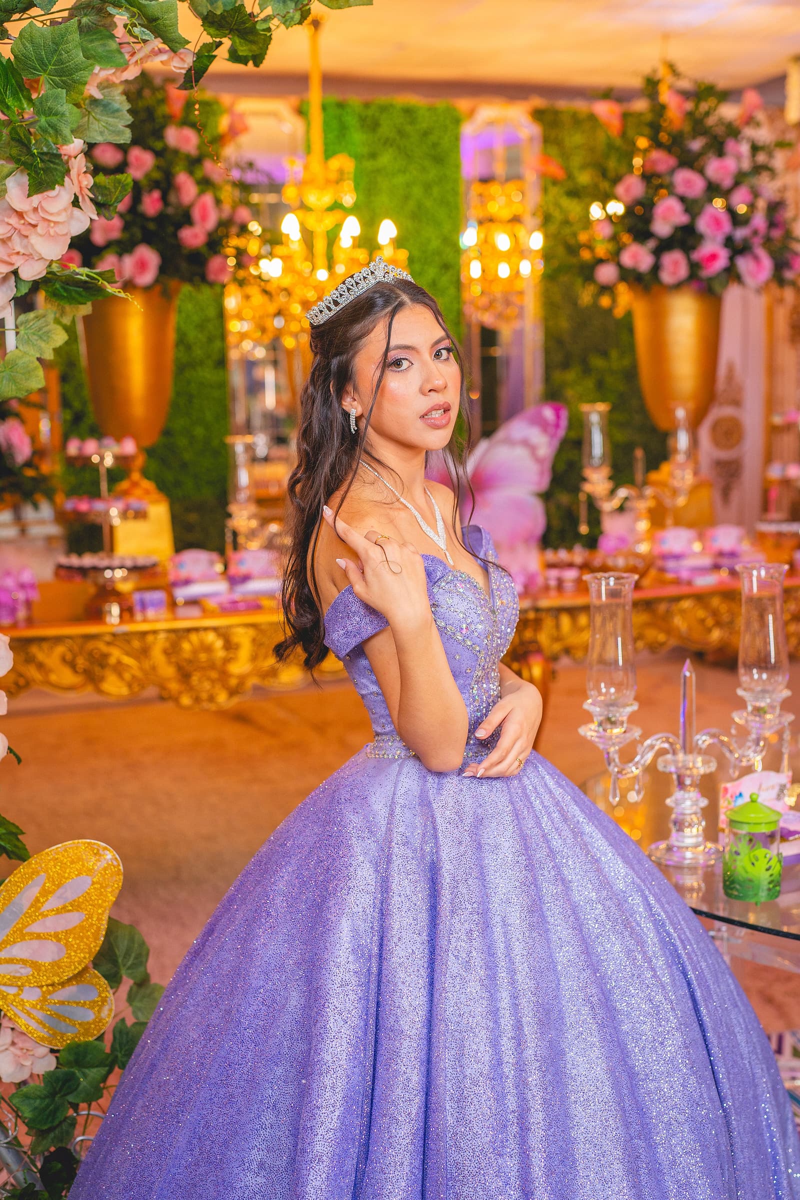 A quinceañera in a lavender ball gown beside the decorated dessert table at her reception