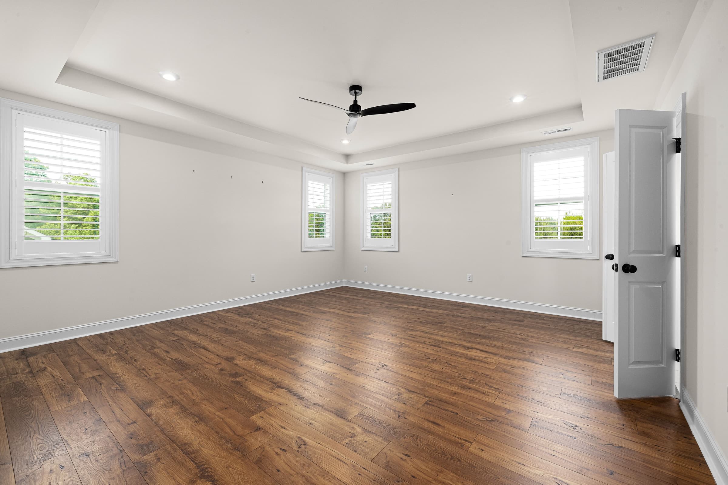 An empty bedroom with wooden floors and shuttered windows photographed for a property listing