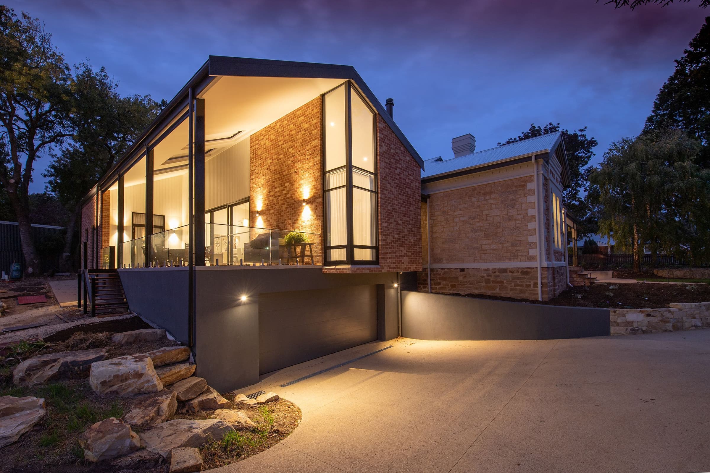 A modern brick and glass house photographed at twilight with warm interior lights showing through the windows