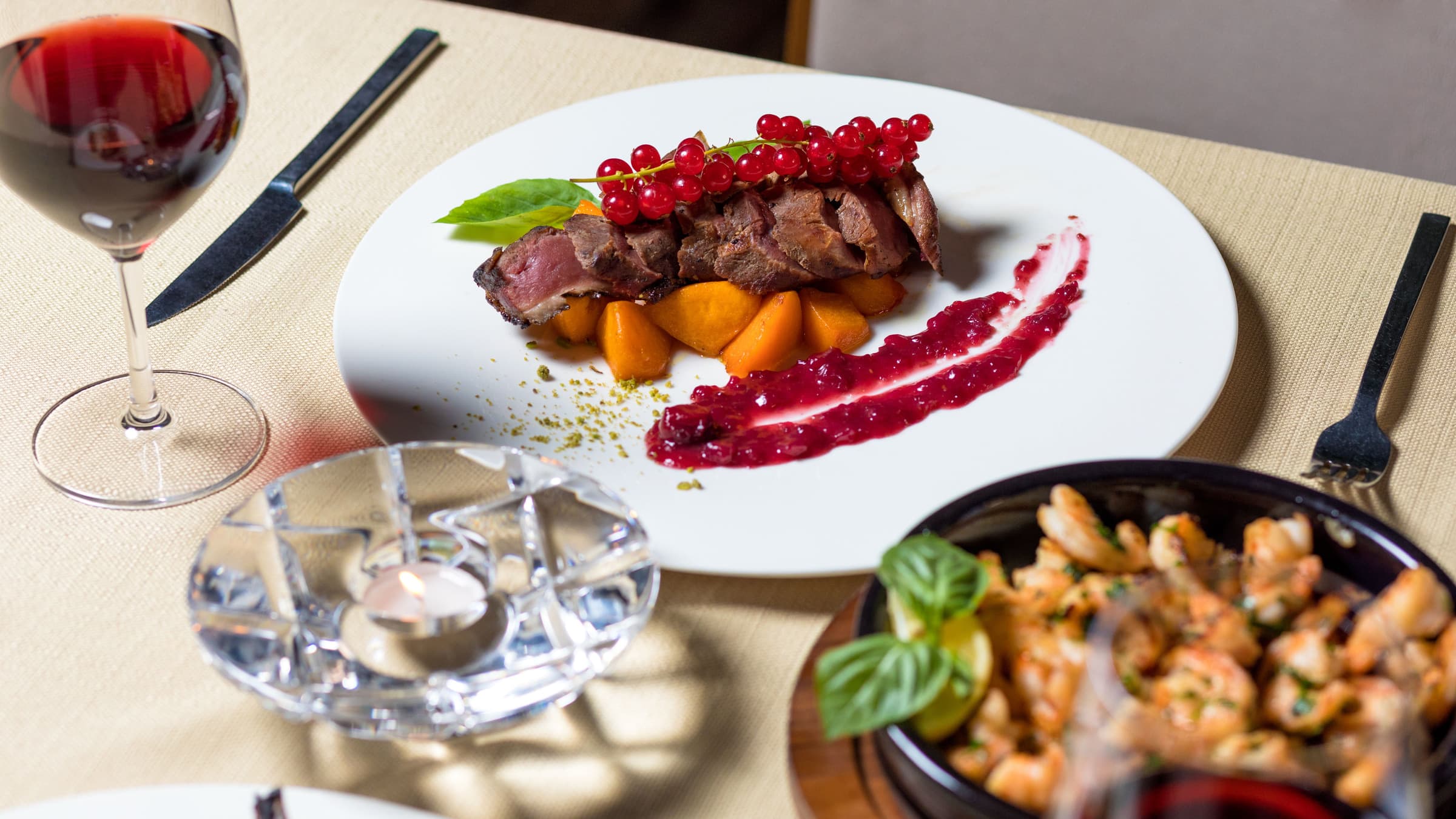 A plated fine dining dish with red currants and a glass of wine on a restaurant table