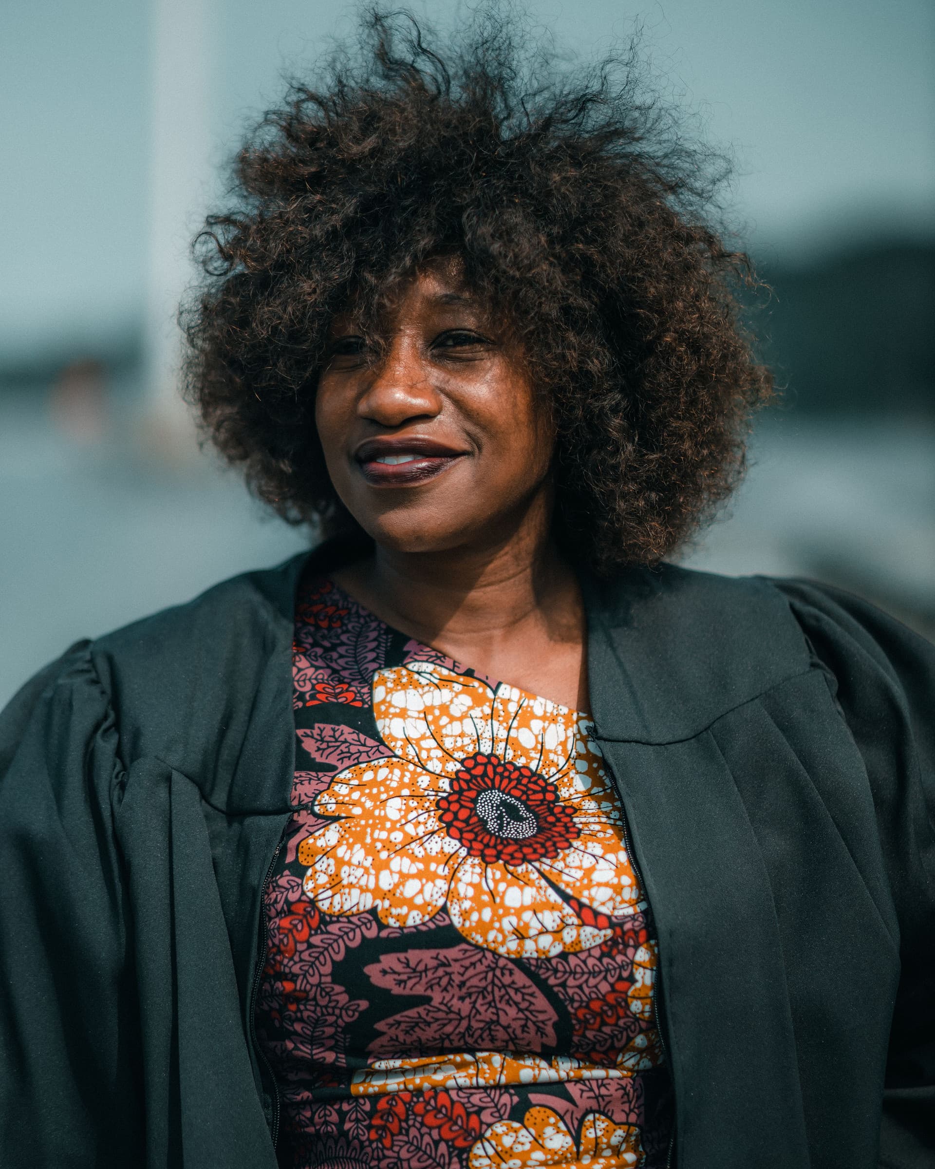 A graduating senior in a cap and gown photographed outdoors on a bright day