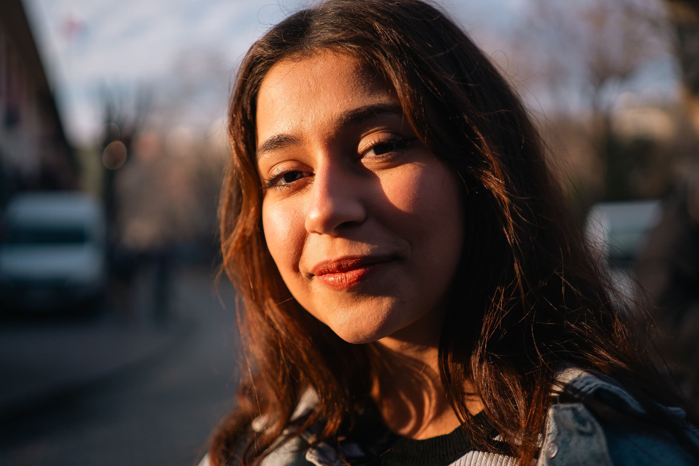 A high school senior smiling in warm evening light on a city street during a senior portrait session