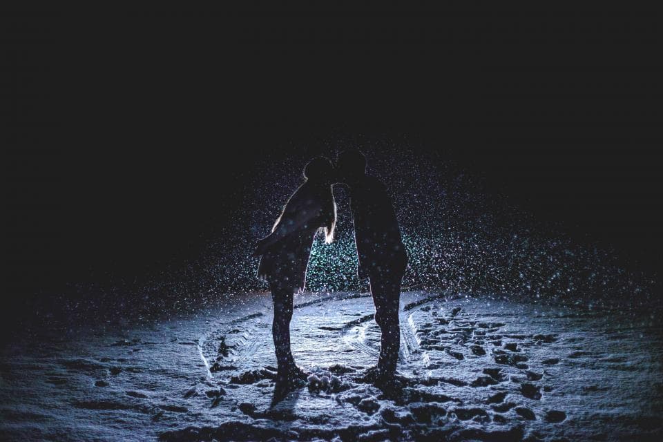 A couple silhouetted close together in falling snow at night