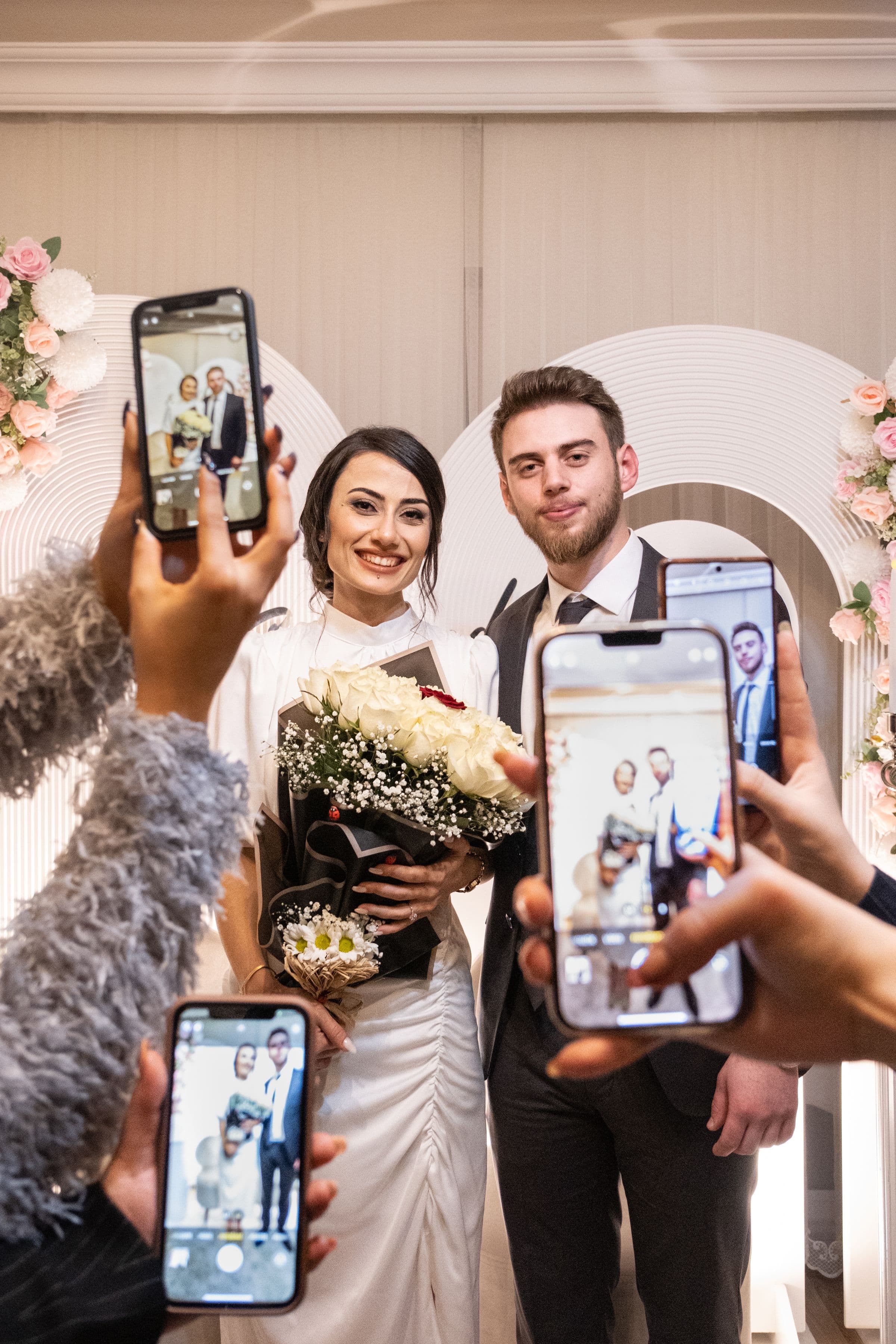 Wedding guests holding up smartphones to photograph a bride and groom during their ceremony