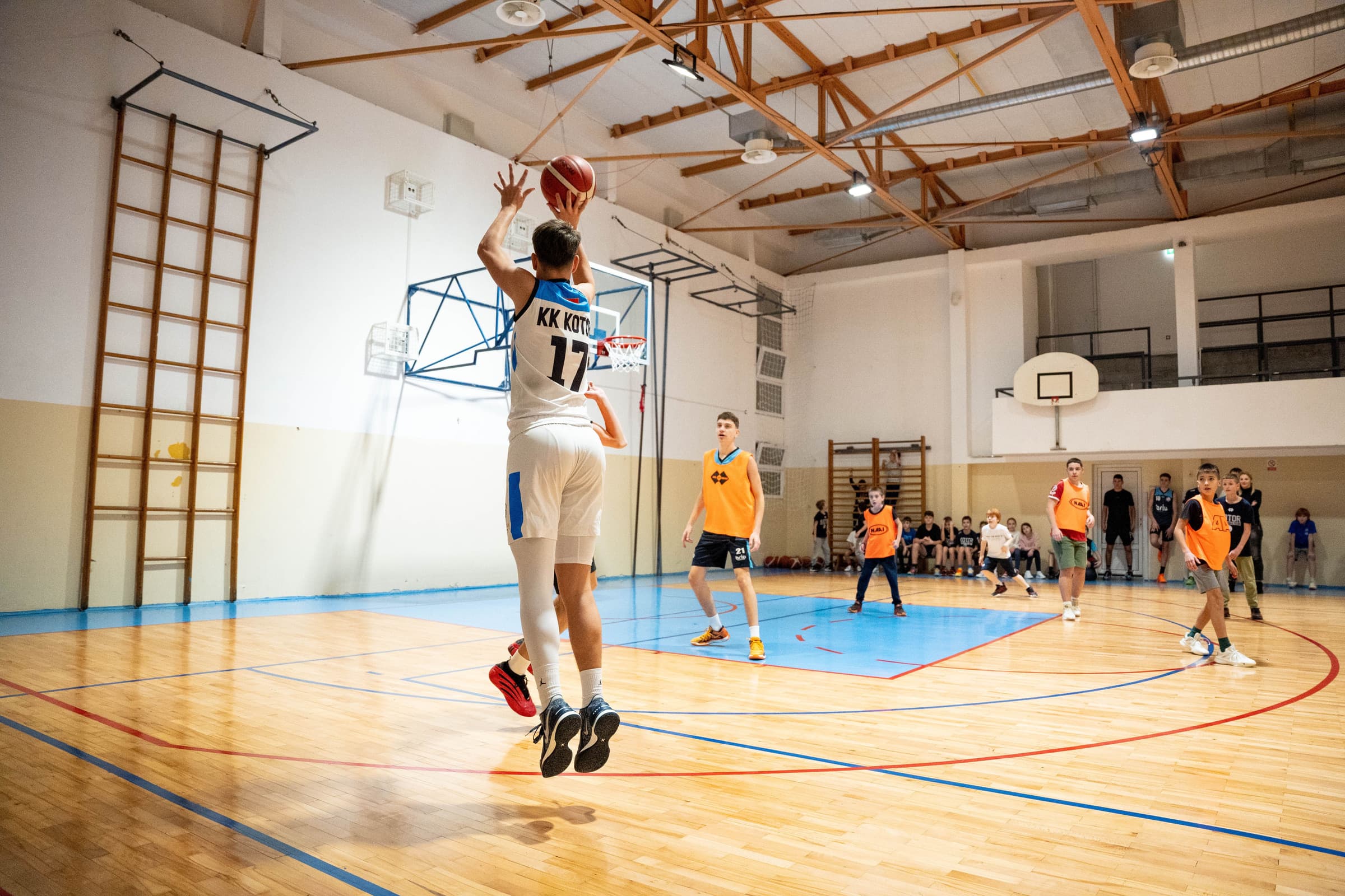 A teenager shooting a basketball during an indoor practice game in a school gym