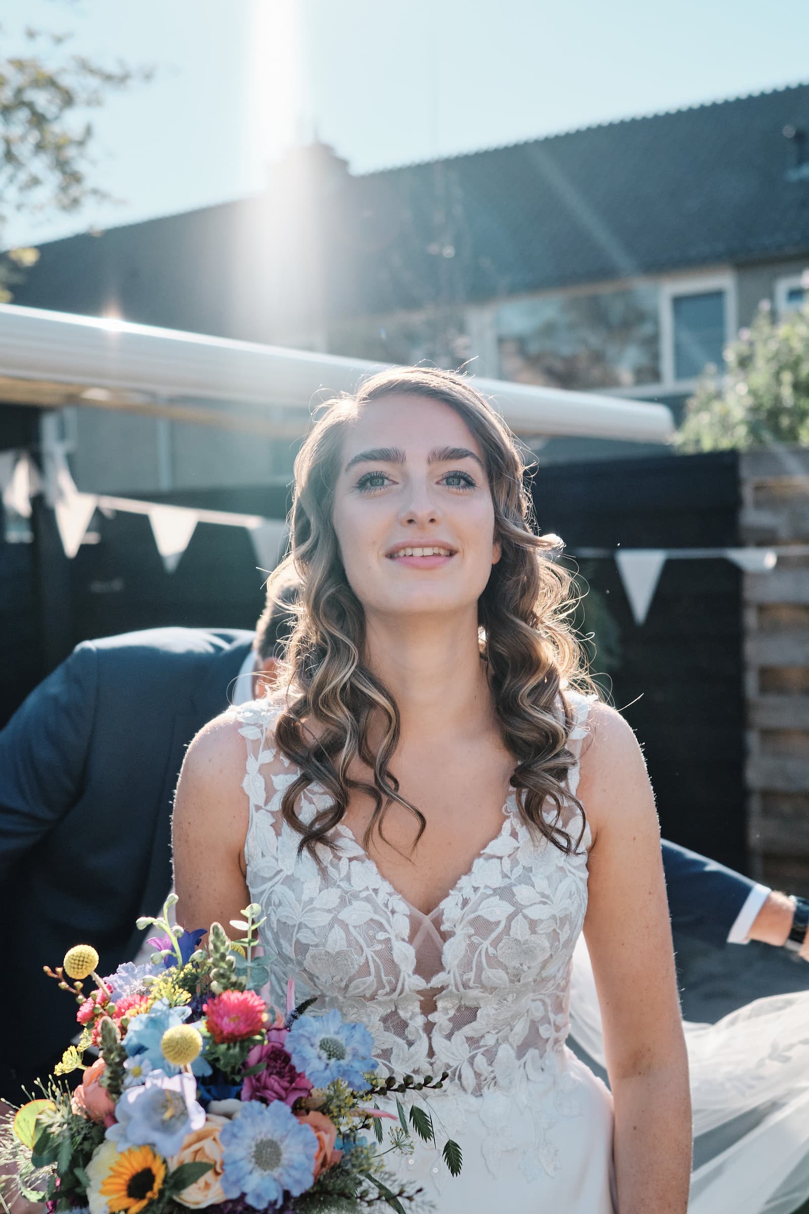 A bride under a willow tree holding a colourful bouquet