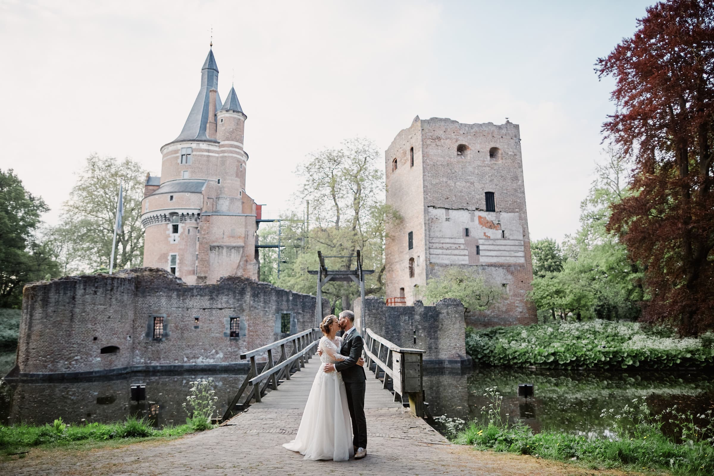 A couple kissing on a wooden bridge in front of a moated castle at dusk