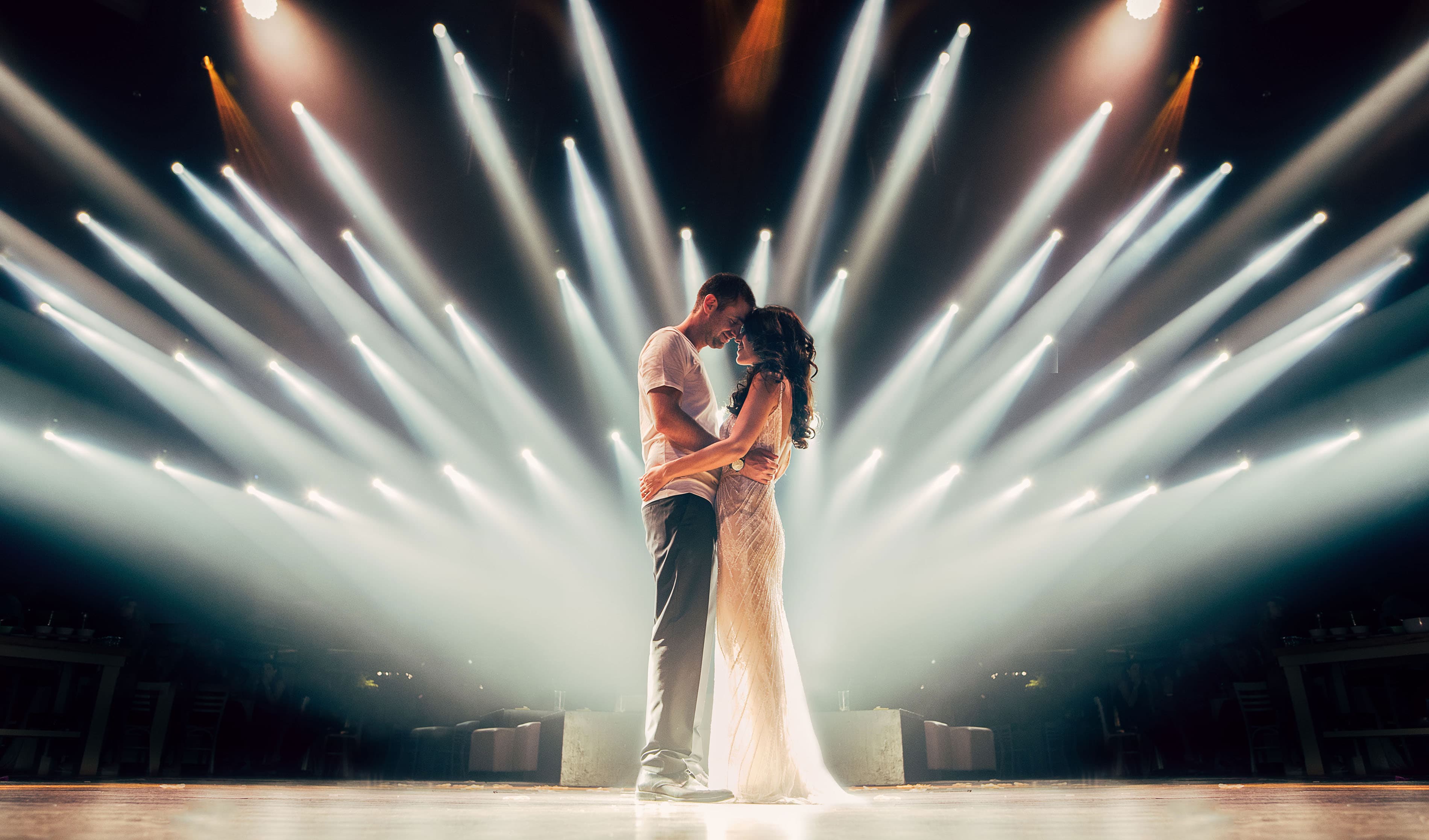 A couple sharing a close dance under dramatic stage lighting at their indoor wedding reception