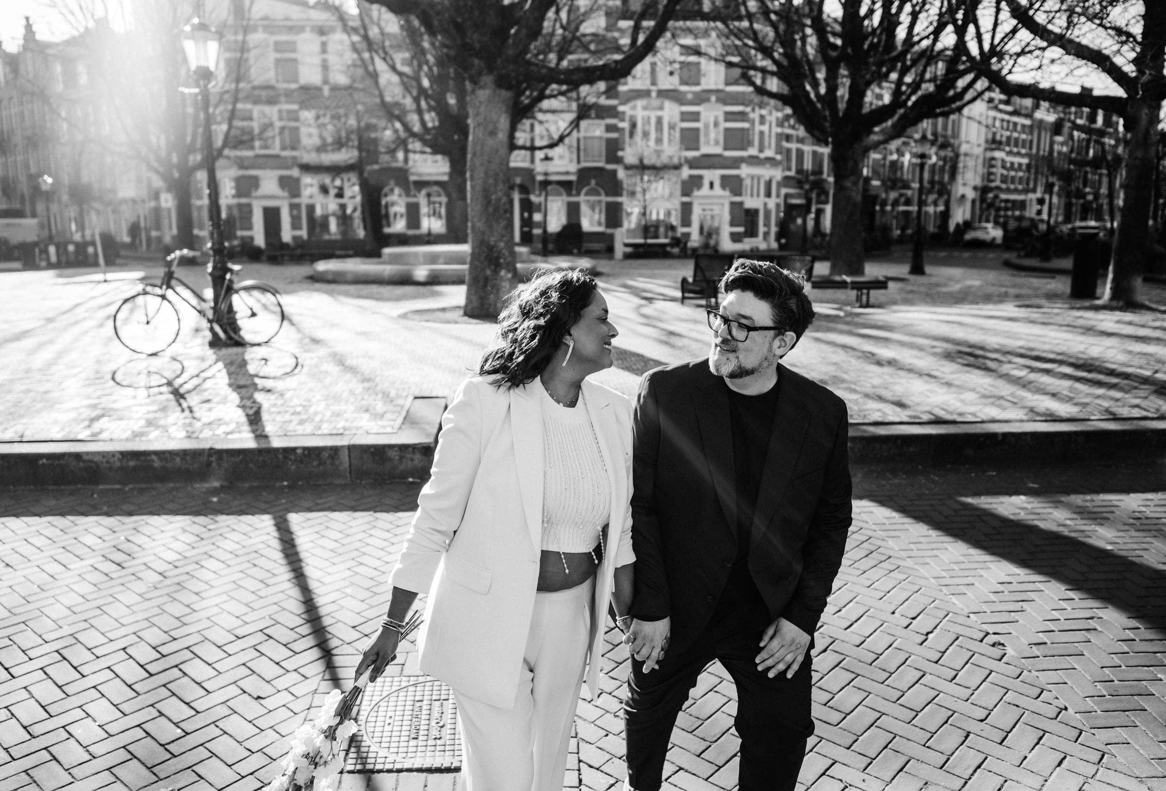 A wedding couple crossing a plaza in Amsterdam at golden hour