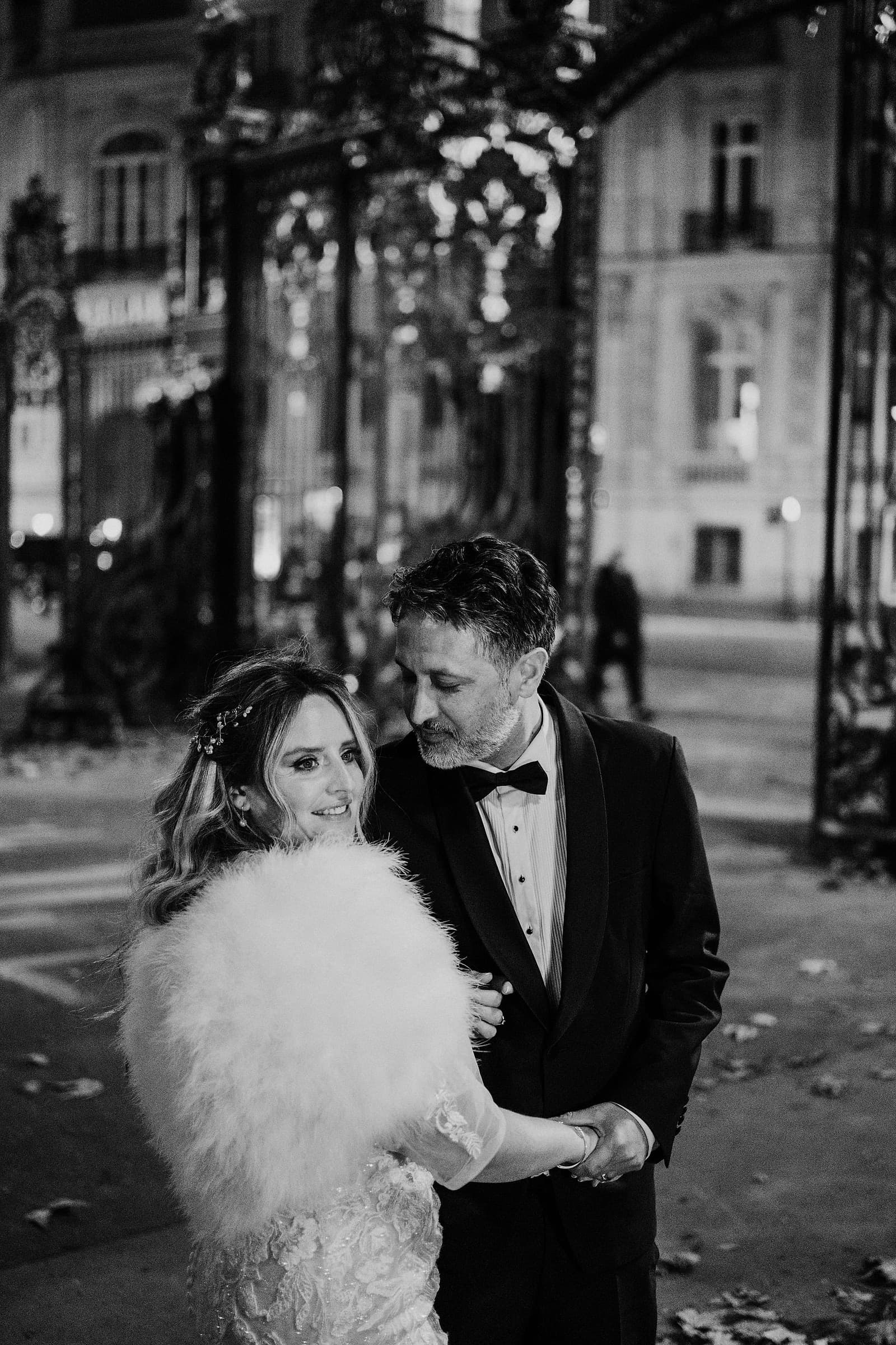 A bride and groom sharing a quiet moment at night beside an ornate iron gate in Paris