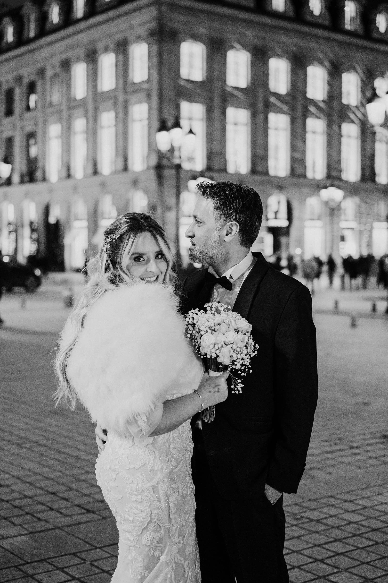 A bride and groom pause together at night in front of an elegant Parisian building